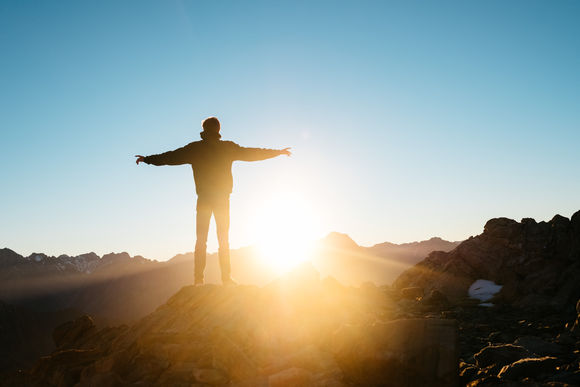 Mensch auf einem Berg vor der Sonne